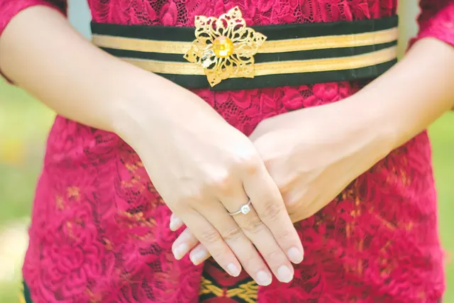 A woman's hands resting on a red lace dress with a decorative belt. Affordable engagement rings for people who want the details