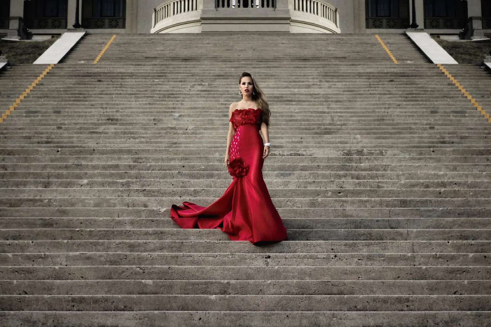 Fashionable woman in a stunning red dress gracefully posing on a grand staircase. What Is the TIFF Red Carpet Dress Code, Really?