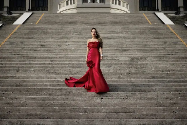 Fashionable woman in a stunning red dress gracefully posing on a grand staircase. What Is the TIFF Red Carpet Dress Code, Really?